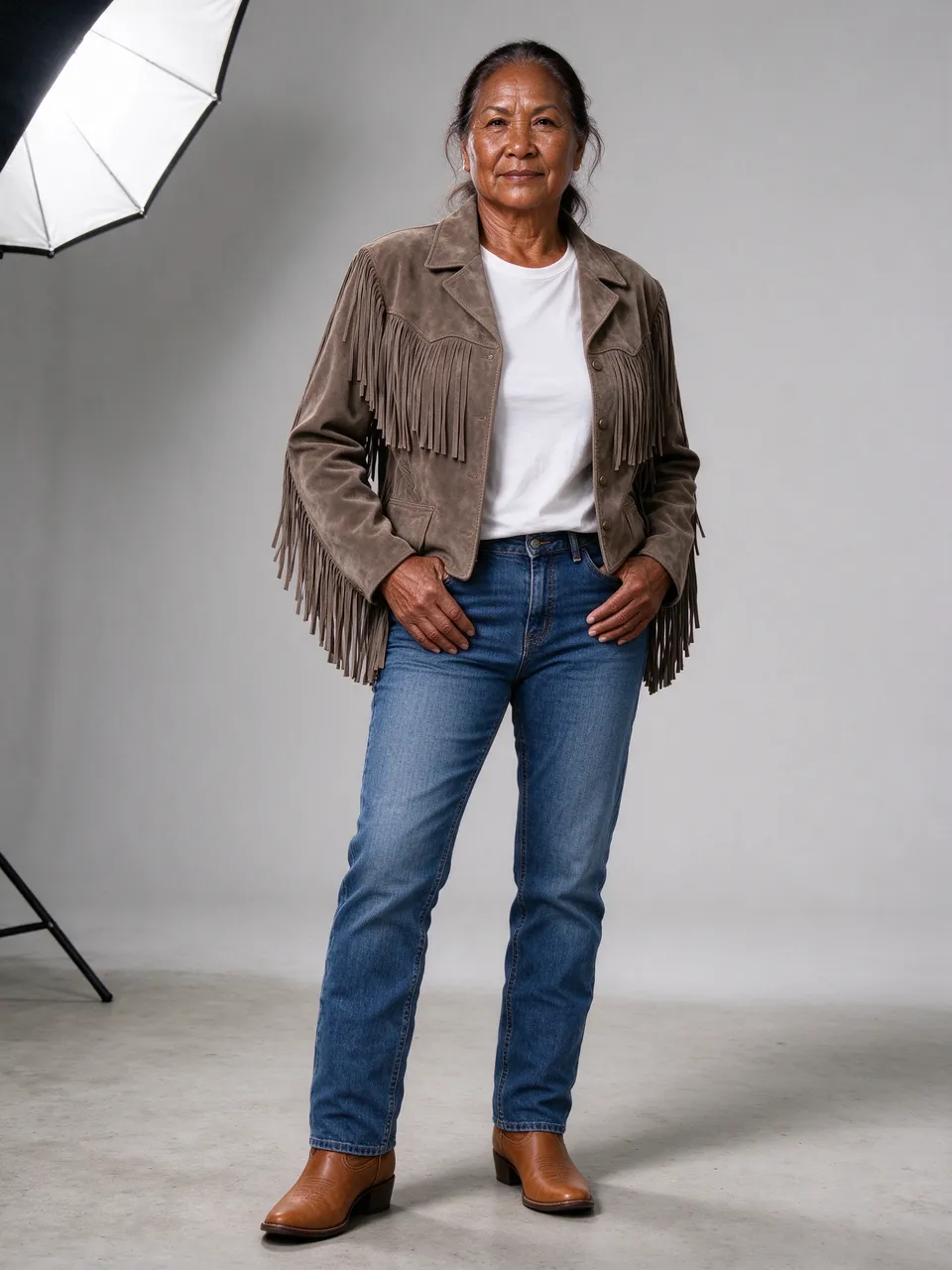 A senior Pacific Islander woman in western wear stands in a photography studio looking at the camera.