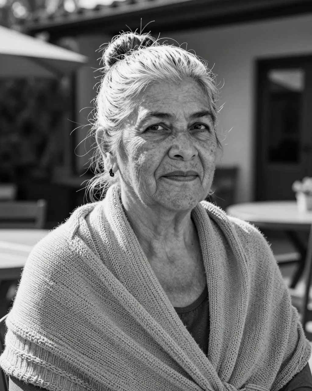 Black and white close-up portrait of an elderly woman in a knit shawl sitting on a sunlit patio