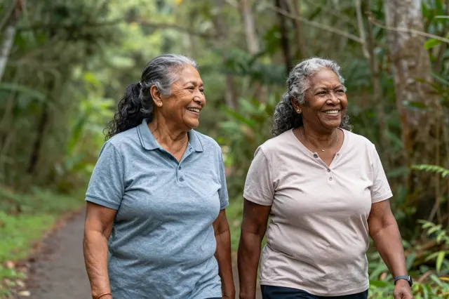 Two smiling senior women walk side by side along a lush green forest path