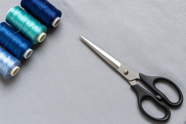Top-down view of thread spools and scissors resting on smooth gray fabric