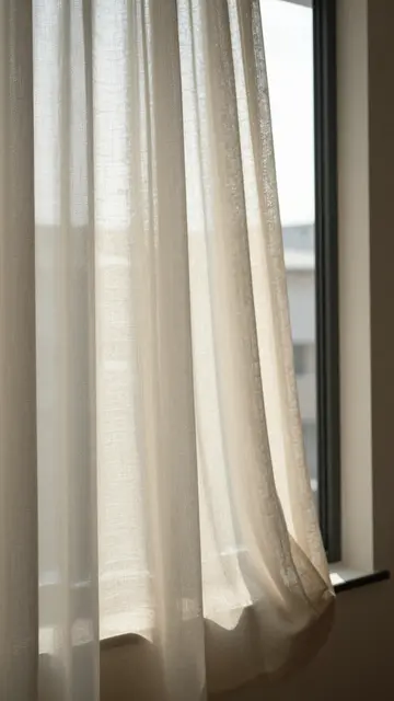 Soft morning sunlight filters through a flowing sheer linen curtain beside a window.