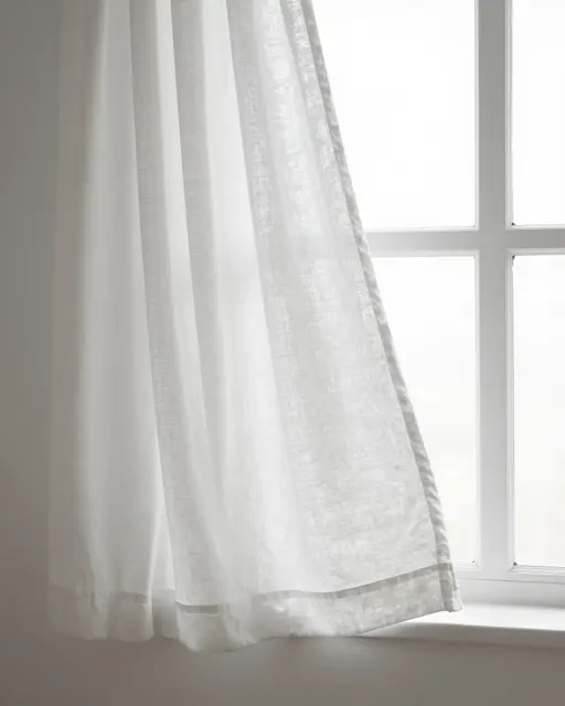 Soft white linen curtain hangs beside a bright paned window, catching gentle diffused light.
