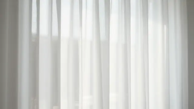 Soft backlight glows through lightweight sheer white hanging curtains