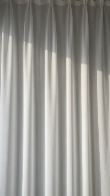 Soft backlit sheer white draped curtain provides neutral vertical copy space