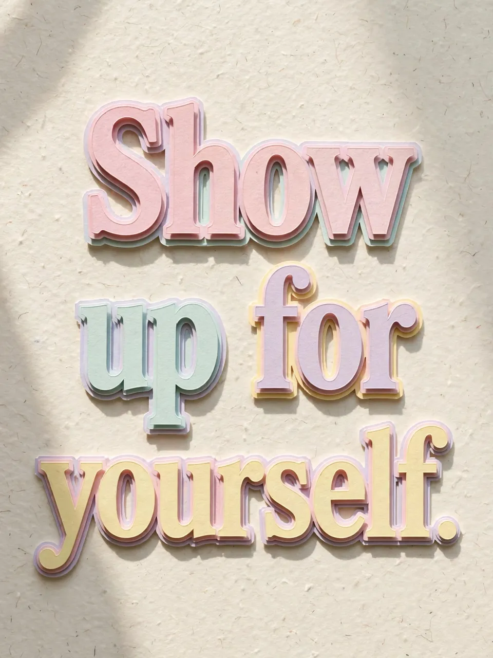 Layered pastel paper cut-out lettering reads "Show up for yourself." with soft shadows on a pale textured background.