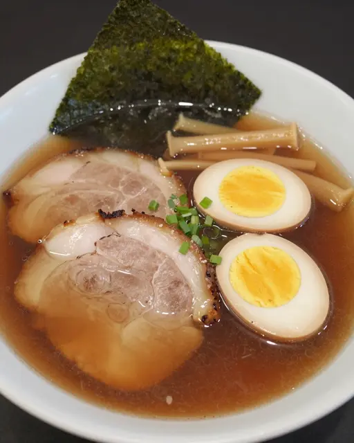 A close-up of a bowl of shoyu ramen topped with chashu, soft egg, nori and menma in clear brown broth