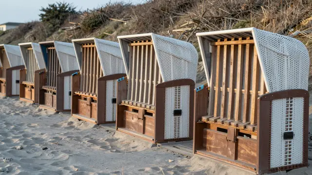 Row of closed hooded beach huts lined on a quiet sandy shore under cool morning light