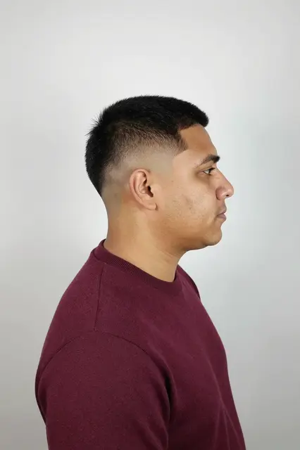 Side profile studio portrait of a Latino man in a burgundy sweater against a plain light backdrop