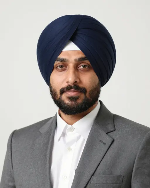 Studio headshot of a South Asian Sikh man in a navy turban and gray suit against a plain white backdrop