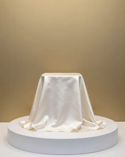 Ivory silk fabric draped over a display podium against a warm champagne wall with copy space