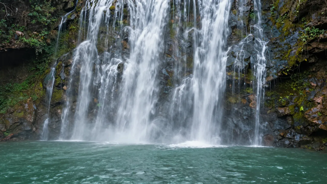 Long exposure view of a broad curtain waterfall flowing over mossy rock into an emerald pool
