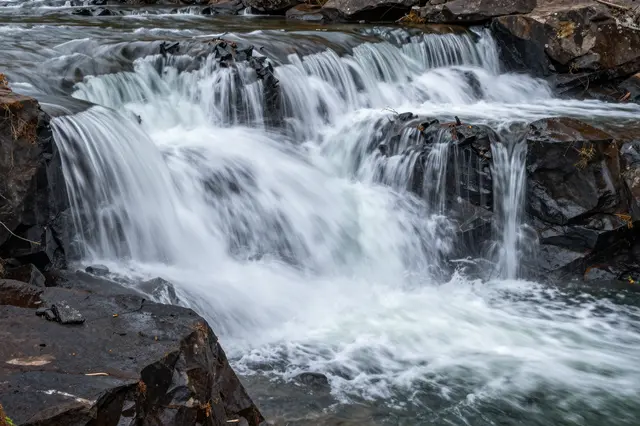 Long exposure shot of smooth flowing water cascading over dark wet basalt rock ledges