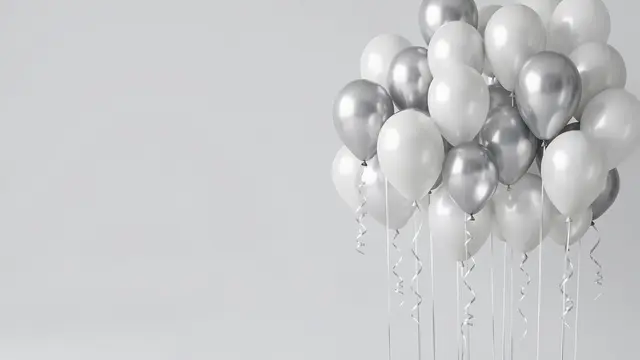 Cluster of metallic silver and matte white balloons with curled ribbons sits on the right of a pale gray backdrop with empty
