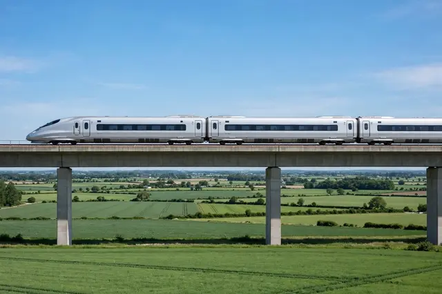 Side view of a sleek silver high-speed train traveling on an elevated concrete viaduct over green farmland under a clear
