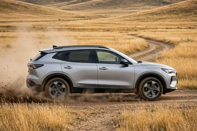 Side view of a silver modern SUV driving on a dirt track kicking up dust through golden grassland