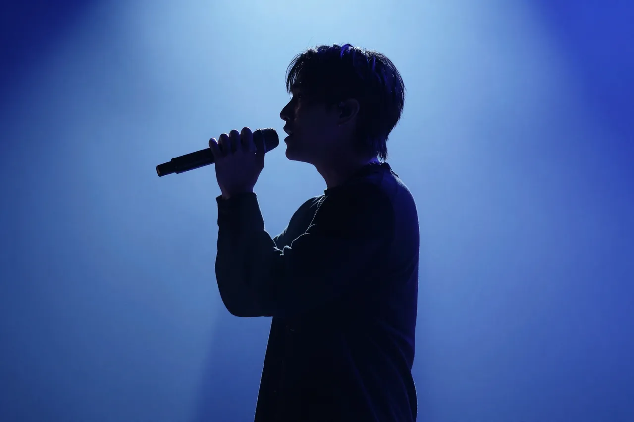 Side profile silhouette of a singer holding a microphone under glowing blue stage lighting