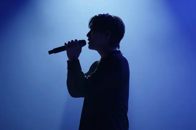 Side profile silhouette of a singer holding a microphone under glowing blue stage lighting