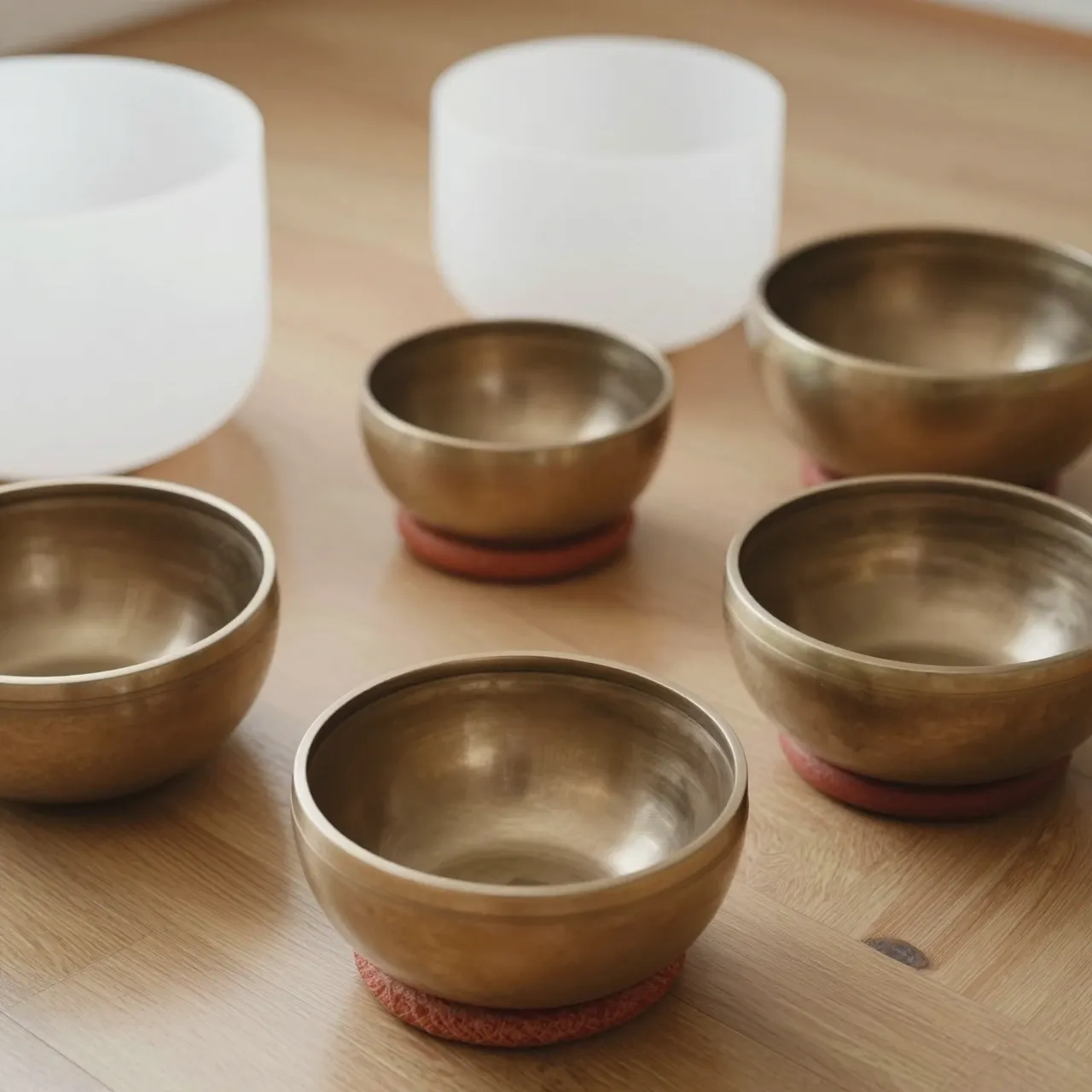 Frosted crystal and brass singing bowls of varying sizes rest on a warm wooden floor