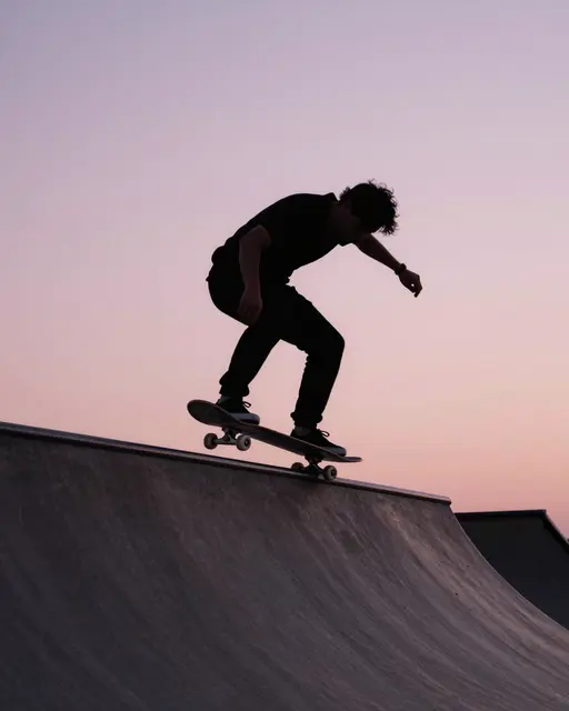 Silhouette of an adult skateboarder balancing on a ramp lip against a soft pink dusk sky