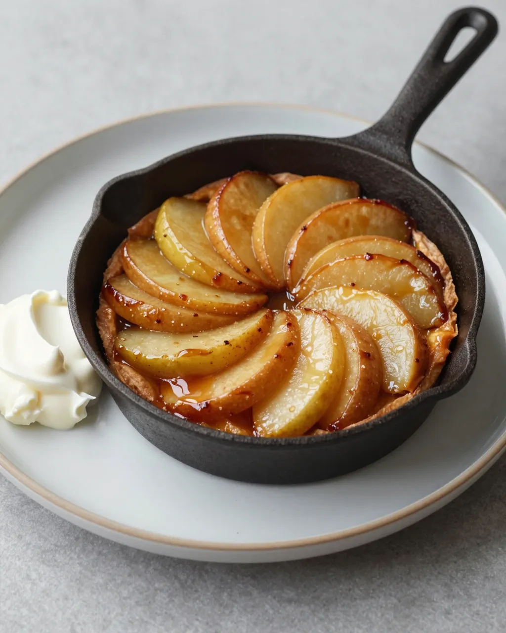 Caramelized apple tarte tatin in a cast iron skillet on a plate alongside crème fraîche