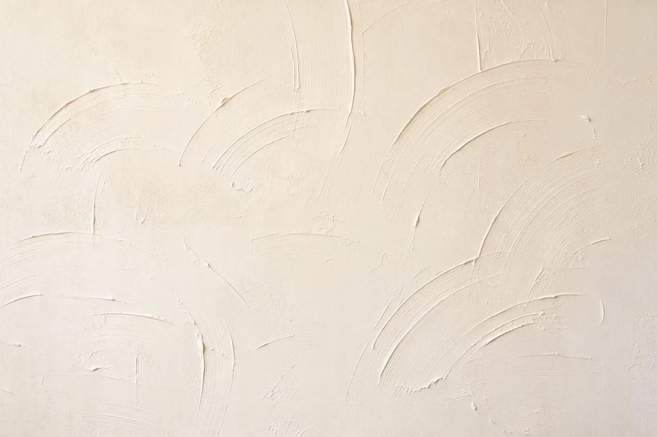 Full frame close-up of textured cream drywall with curved skip trowel compound strokes lit by soft raking light