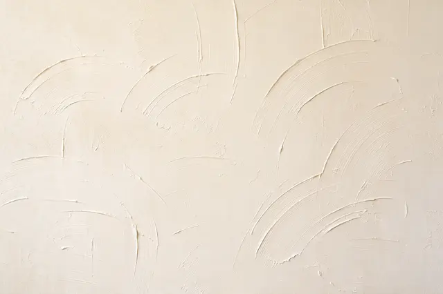 Full frame close-up of textured cream drywall with curved skip trowel compound strokes lit by soft raking light
