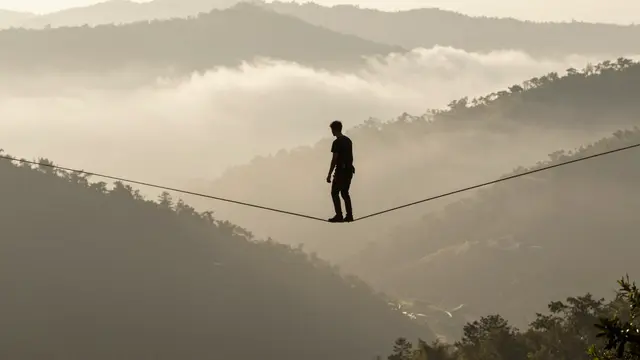 Silhouetted slackliner balances on a high line over misty forested mountains at golden sunrise