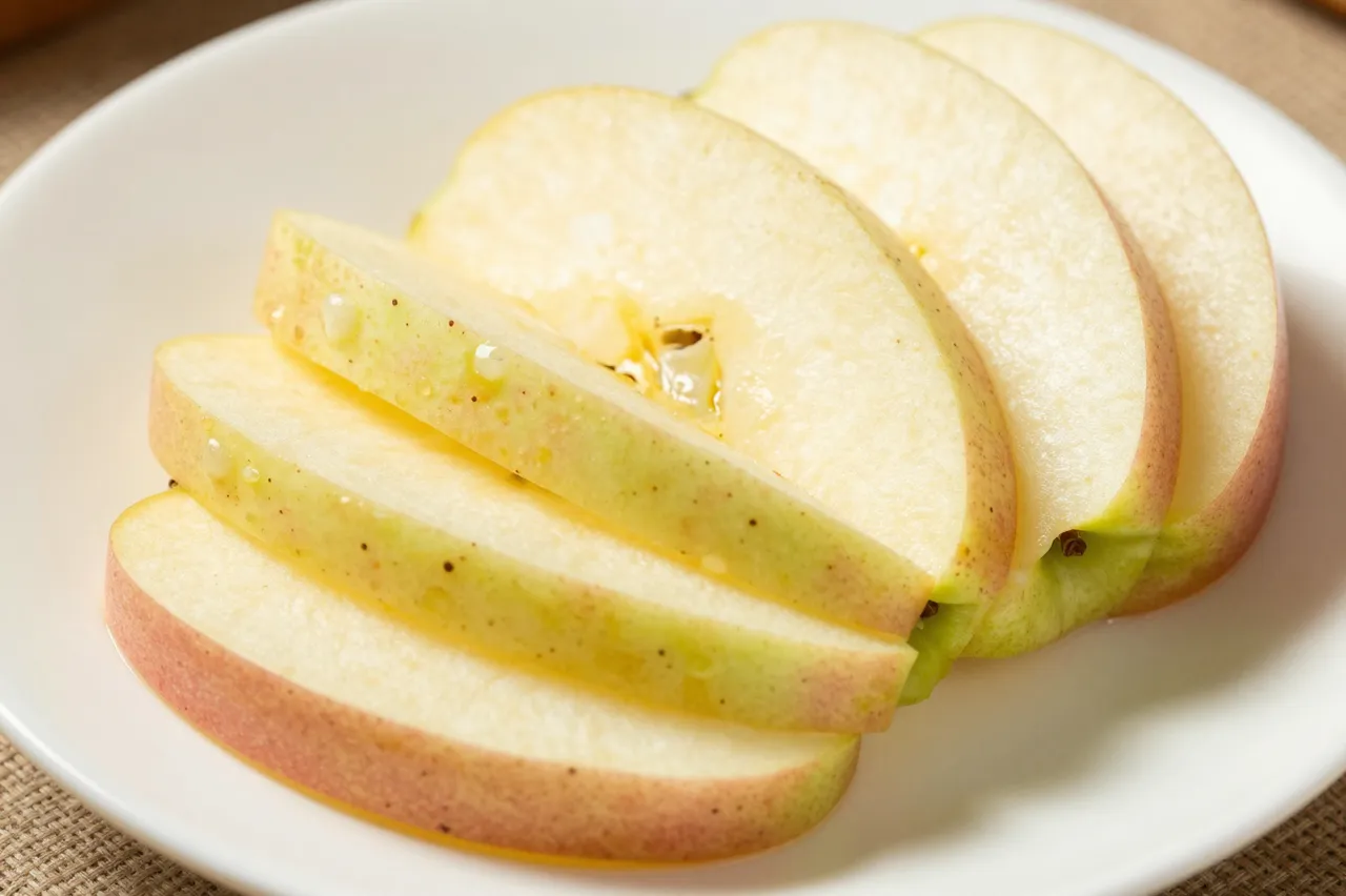 Fanned fresh apple slices resting on a plain white plate with glistening juice droplets