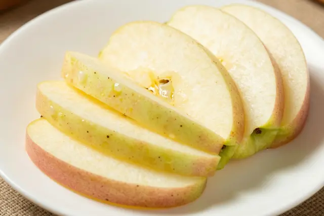 Fanned fresh apple slices resting on a plain white plate with glistening juice droplets