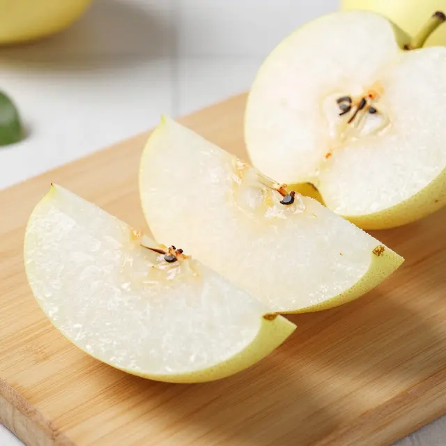 Fresh sliced asian pear wedges and a halved pear rest on a light wooden cutting board.