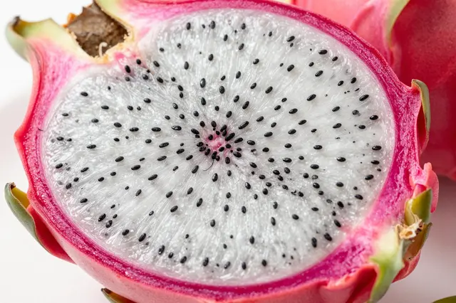 Close-up of a halved white-fleshed dragon fruit showing tiny black seeds on a light surface