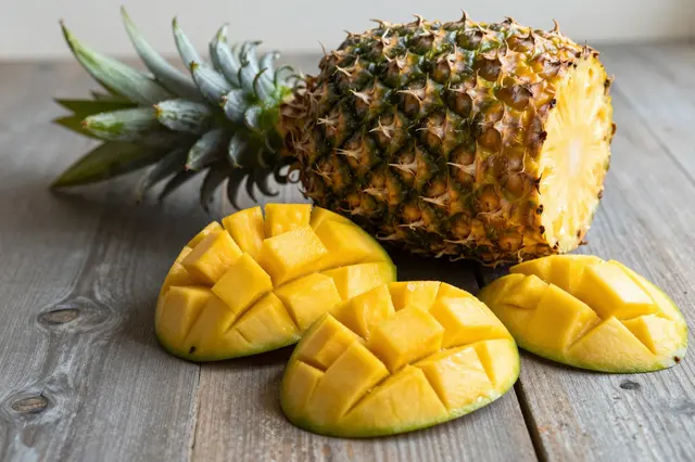 Cut pineapple and cubed sliced mango arranged on a weathered wooden table