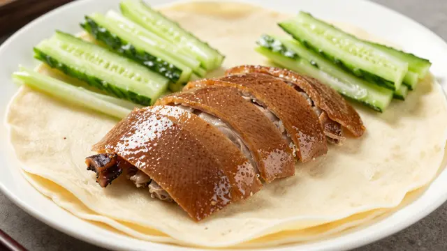 Sliced crispy peking duck arranged with thin pancakes and cucumber strips on a white plate