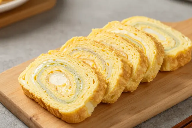 Four sliced pieces of layered rolled omelette arranged neatly on a small wooden serving board