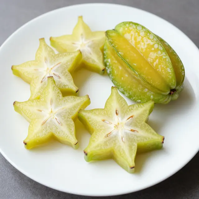 Star-shaped sliced starfruit and a partial whole starfruit rest on a plain white plate over a gray surface.