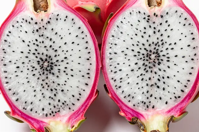 Close-up of two halved white-flesh dragon fruit with black seeds resting on a light surface