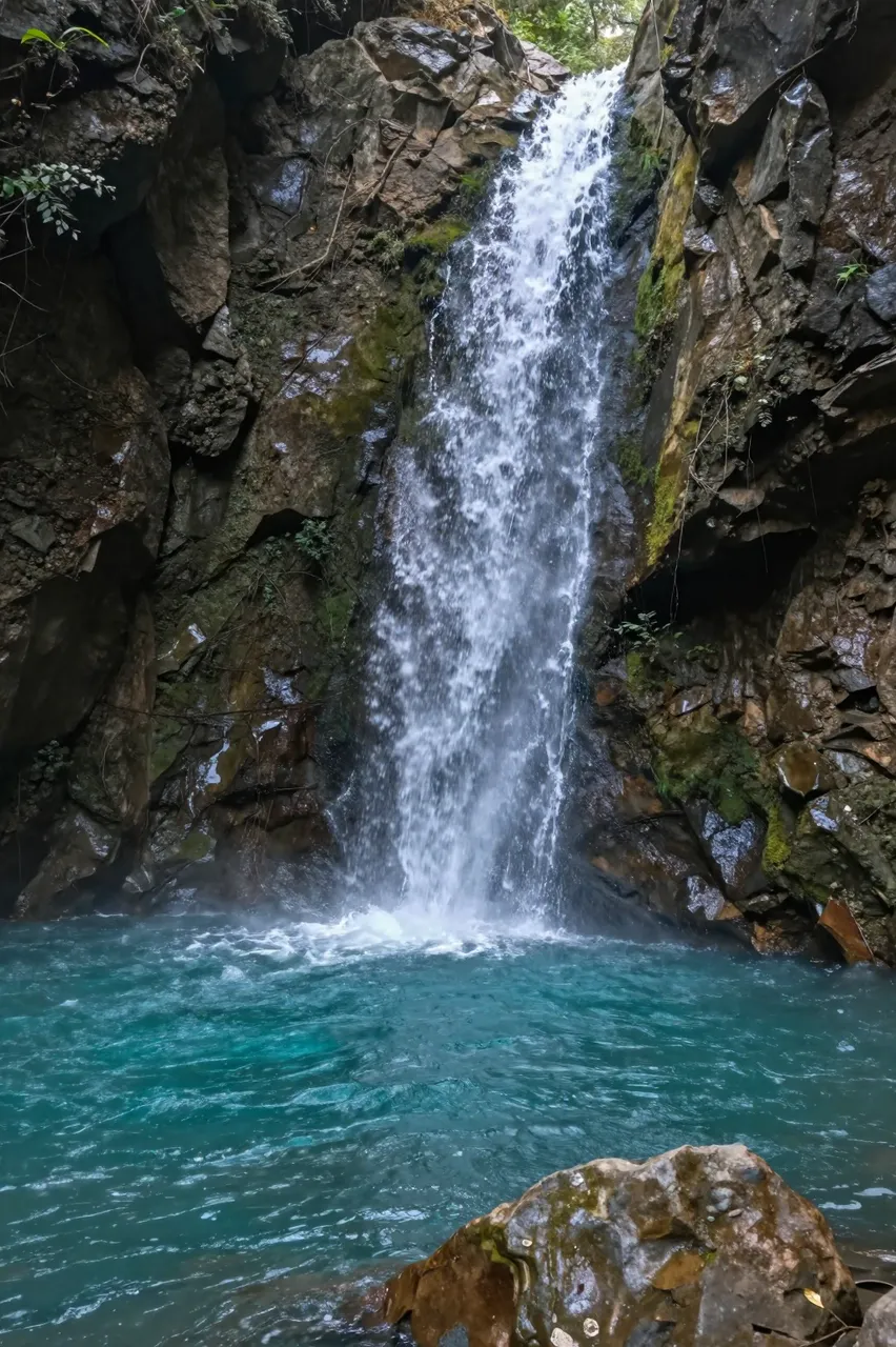 A waterfall cascades down mossy slot canyon rock walls into a bright turquoise pool below.