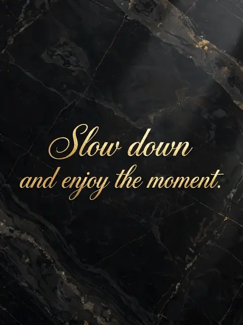 Gold foil script reading "Slow down and enjoy the moment." on polished black marble with natural veining