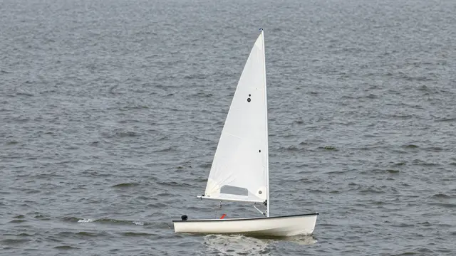 An unmanned small dinghy with a plain white sail floats on choppy gray open water.