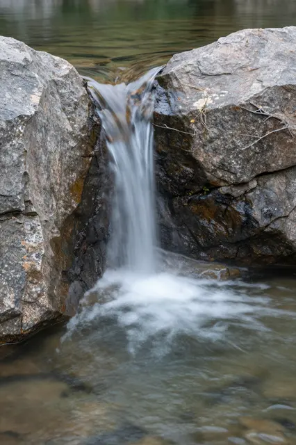 Long exposure shot of a narrow stream spilling between granite boulders into a clear shallow pool