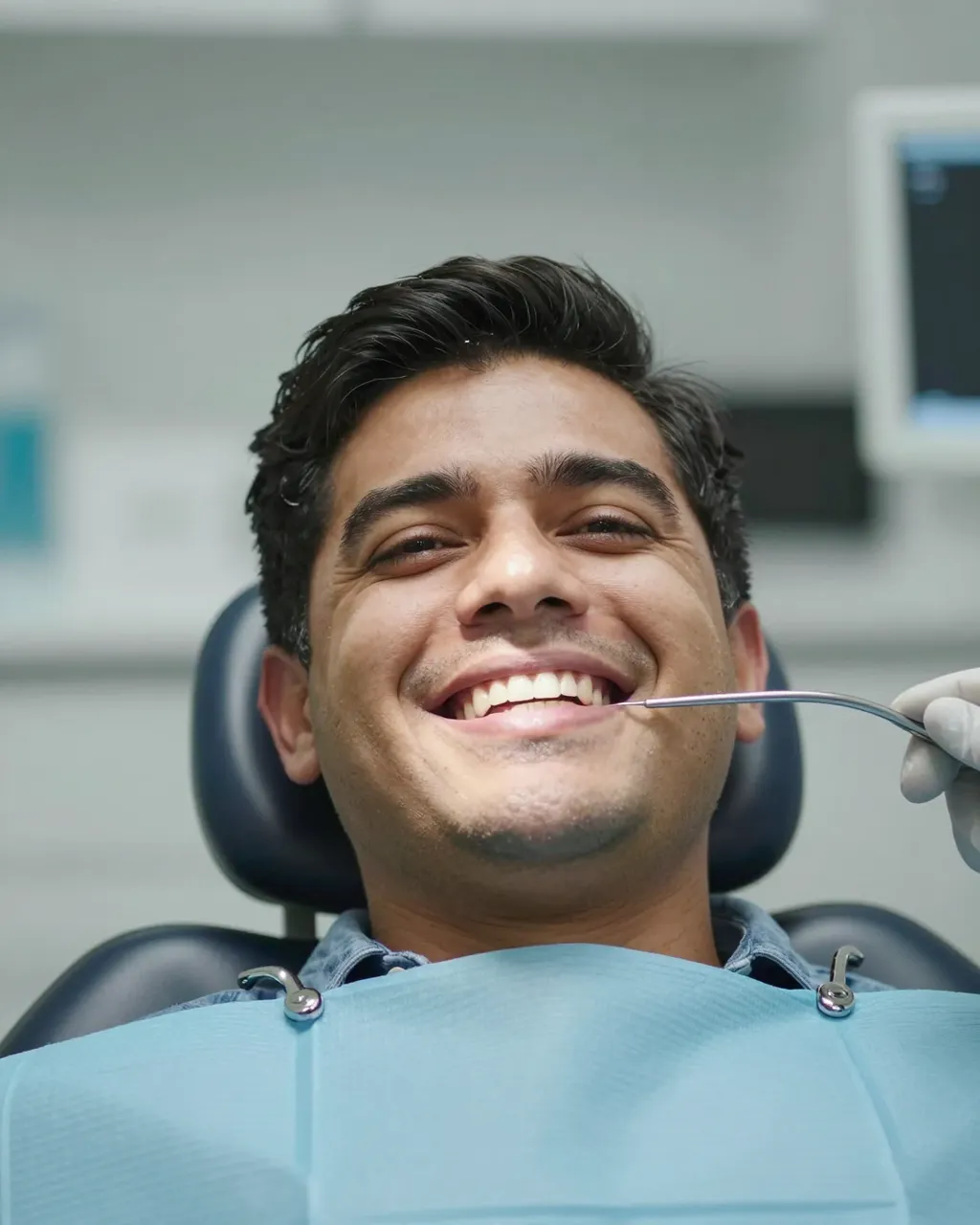 Happy man grins seated in a dental chair as a gloved hand holds a dental mirror near his mouth