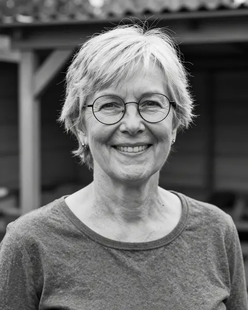 Black and white close-up portrait of a smiling older woman with short silver hair and round glasses, standing outside a