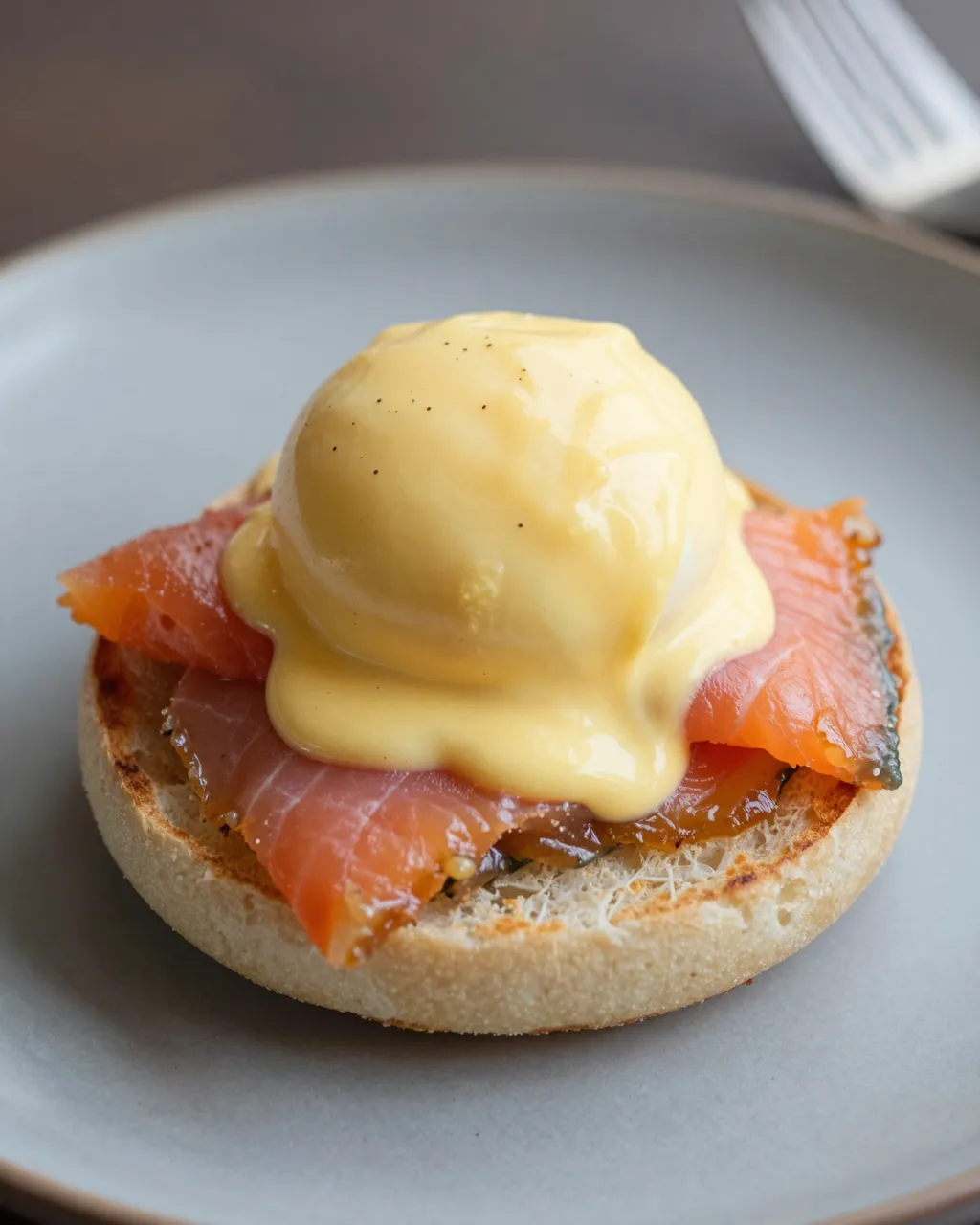 A close-up of eggs royale with hollandaise sauce on an english muffin resting on a gray plate