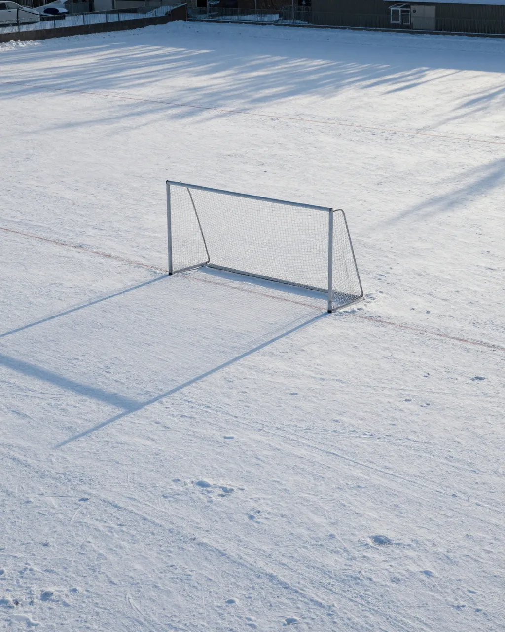 A lone soccer goal sits on a snow-covered empty sports field in soft morning light