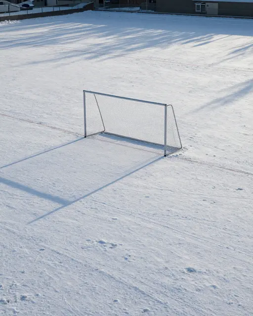 A lone soccer goal sits on a snow-covered empty sports field in soft morning light