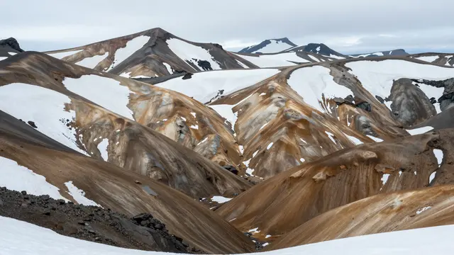 Colorful striated rhyolite mountains dotted with patchy snow stretch across the overcast Icelandic highlands
