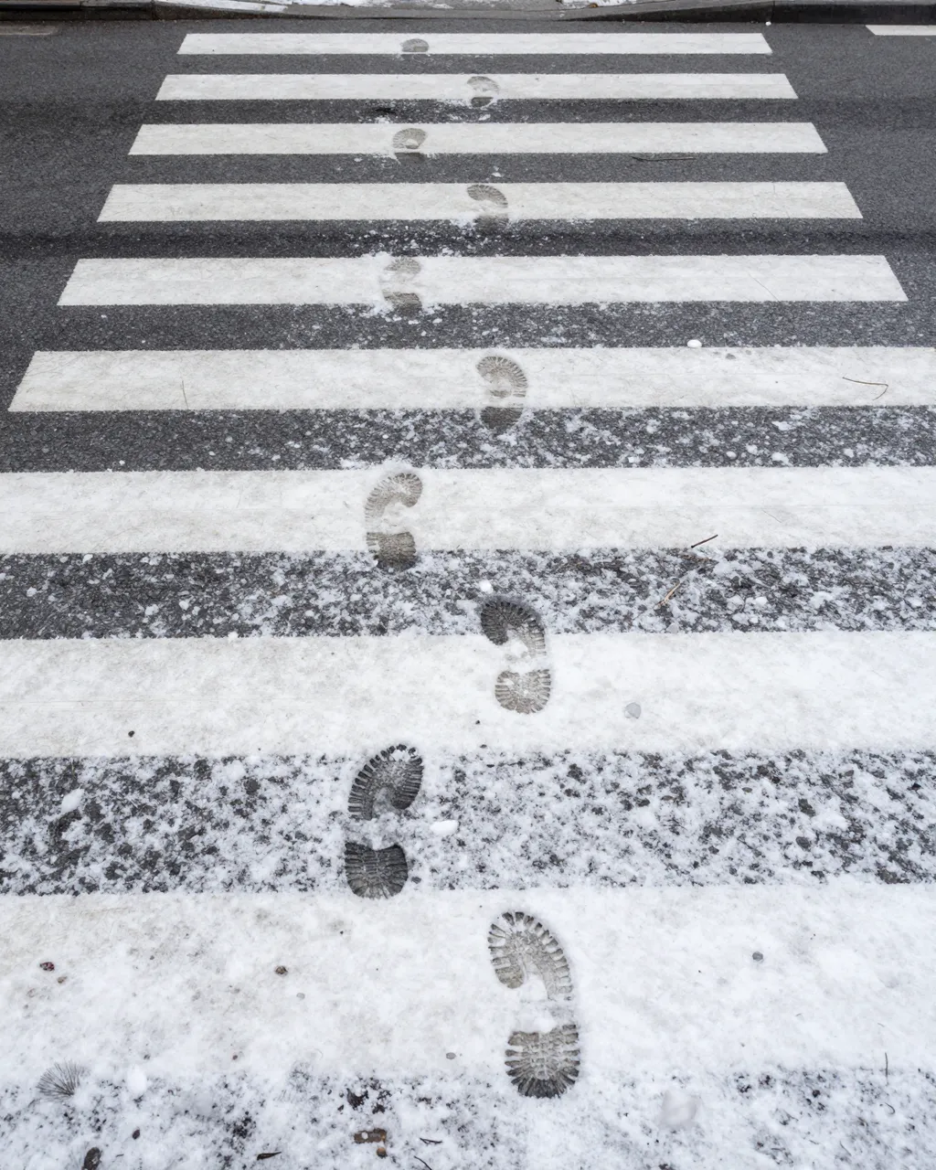 Top-down view of footprints trailing across snow-dusted street crosswalk stripes
