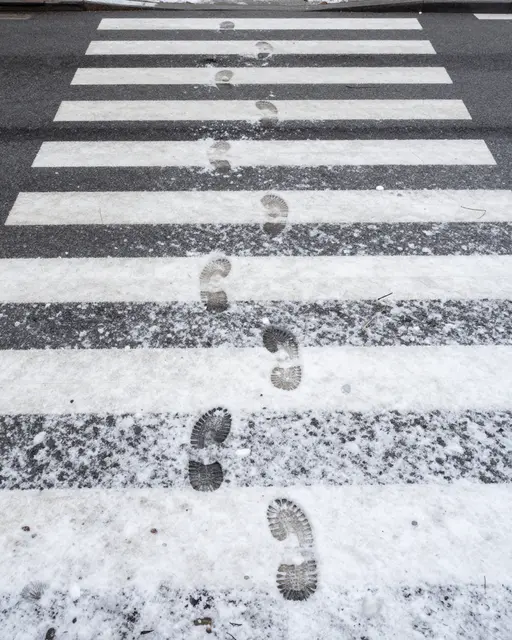 Top-down view of footprints trailing across snow-dusted street crosswalk stripes