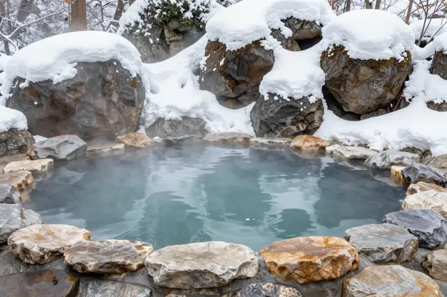 Steaming turquoise hot spring surrounded by snow-covered rocks in a winter Japanese onsen setting