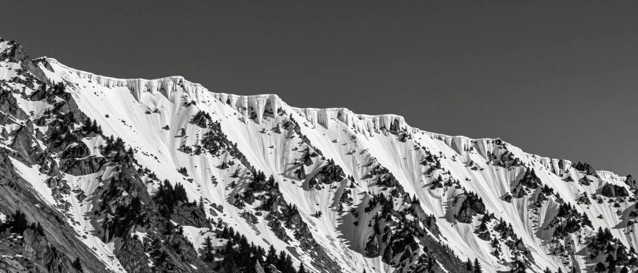 Black and white view of a knife-edge snow cornice mountain ridge under a moody dark sky